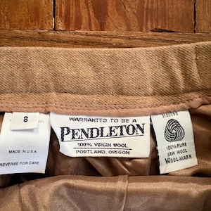 May include: Close-up of the interior waistband of a tan wool skirt. The tags read "PENDLETON" and "100% Virgin Wool." The skirt is size 8 and made in the U.S.A. The lining is a light brown satin.