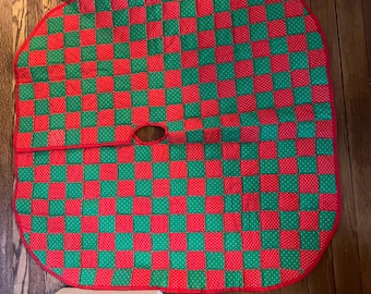 May include: A red and green checkered Christmas tree skirt with a hole in the center for the tree trunk. The skirt is made of quilted fabric with white polka dots.