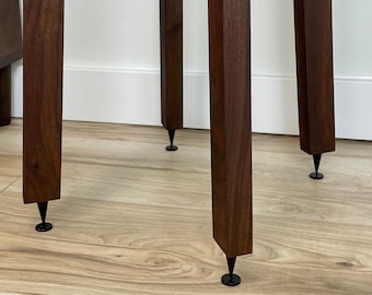 May include: Close-up of three dark brown wooden legs with black metal feet. The legs are square and have a smooth finish.
