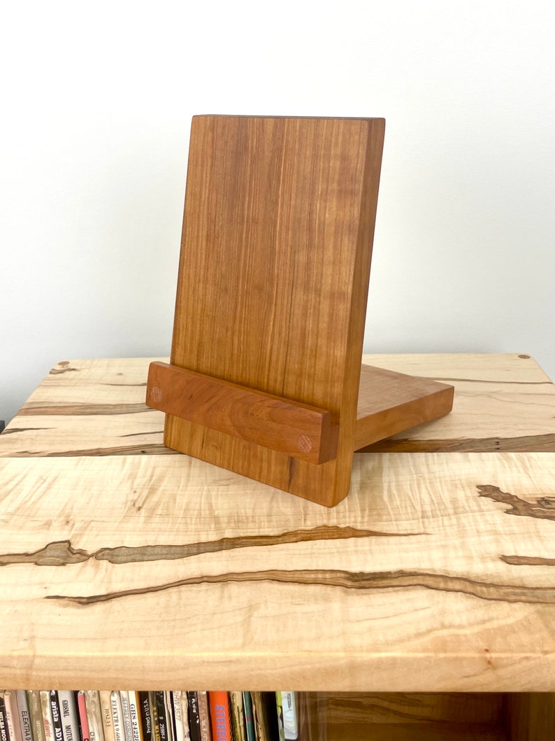 Peut inclure: Un support en bois compos&eacute; d'un panneau arri&egrave;re vertical et d'une tablette horizontale pour maintenir des objets. Le support est fabriqu&eacute; en bois de ton moyen avec un grain visible et deux chevilles en bois circulaires sur le rebord avant.