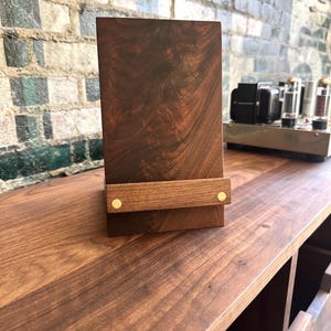 Peut inclure: Un support vertical rectangulaire en bois brun fonc&eacute; dot&eacute; d'une barre de soutien horizontale sur le devant. La barre est fix&eacute;e au corps principal par deux petites attaches m&eacute;talliques circulaires de couleur laiton. Le bois pr&eacute;sente un grain naturel.