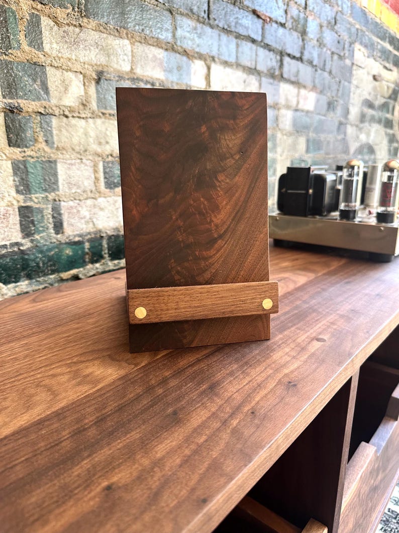 Peut inclure: Un support vertical rectangulaire en bois brun fonc&eacute; dot&eacute; d'une barre de soutien horizontale sur le devant. La barre est fix&eacute;e au corps principal par deux petites attaches m&eacute;talliques circulaires de couleur laiton. Le bois pr&eacute;sente un grain naturel.