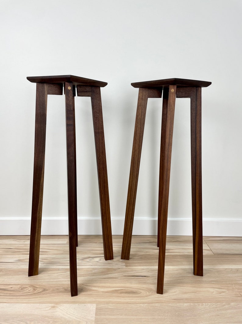 May include: Two dark brown wooden plant stands with a square top and four legs. The stands are made of solid wood and have a simple, modern design.