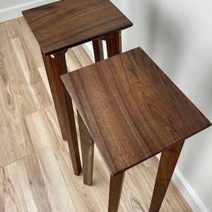 May include: Two wooden nesting tables with a dark brown finish. The tables have a simple design with four legs and a rectangular top.