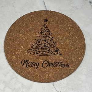 May include: A round cork trivet with a black and white design of a Christmas tree with stars and the text "Merry Christmas".