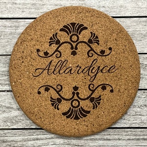 Puede incluir: Un posavasos redondo de corcho con un diseño decorativo y el nombre "Allardyce" grabado en el centro.