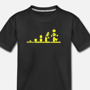 May include: Black t-shirt featuring a yellow graphic depicting the evolution of a Lego minifigure. The graphic shows a series of Lego bricks developing into a Lego minifigure.