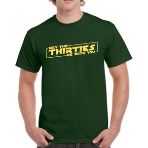 May include: A dark green t-shirt with a yellow graphic that says "May the Thirties Be With You".