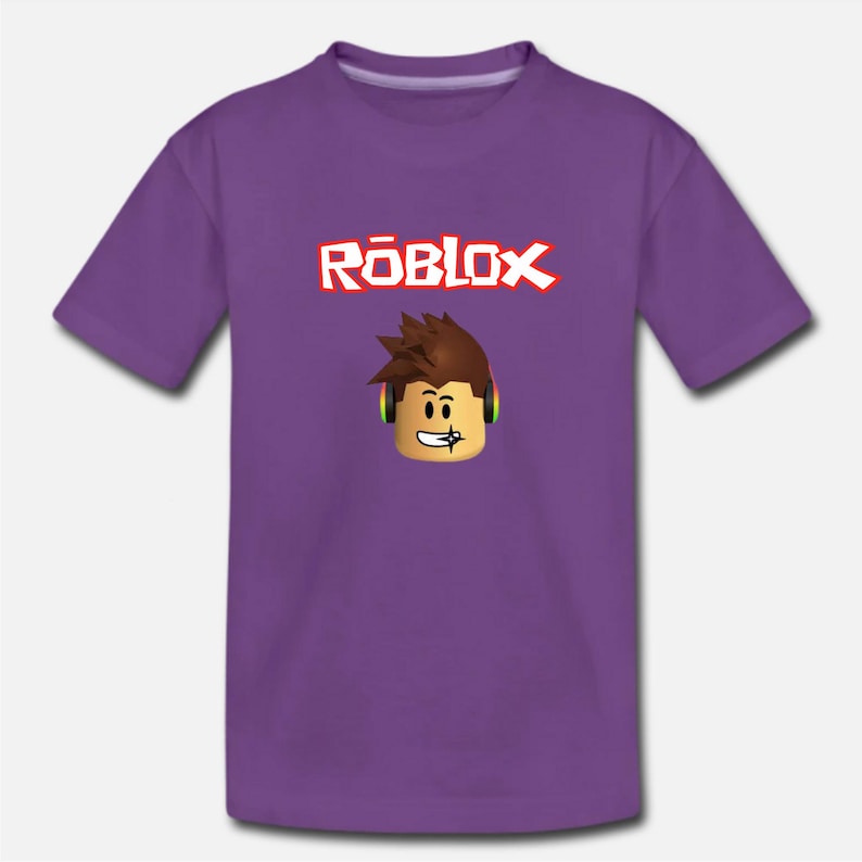 Puede incluir: Camiseta morada para j&oacute;venes con la palabra "ROBLOX" en letras rojas y blancas y un personaje de dibujos animados con auriculares.