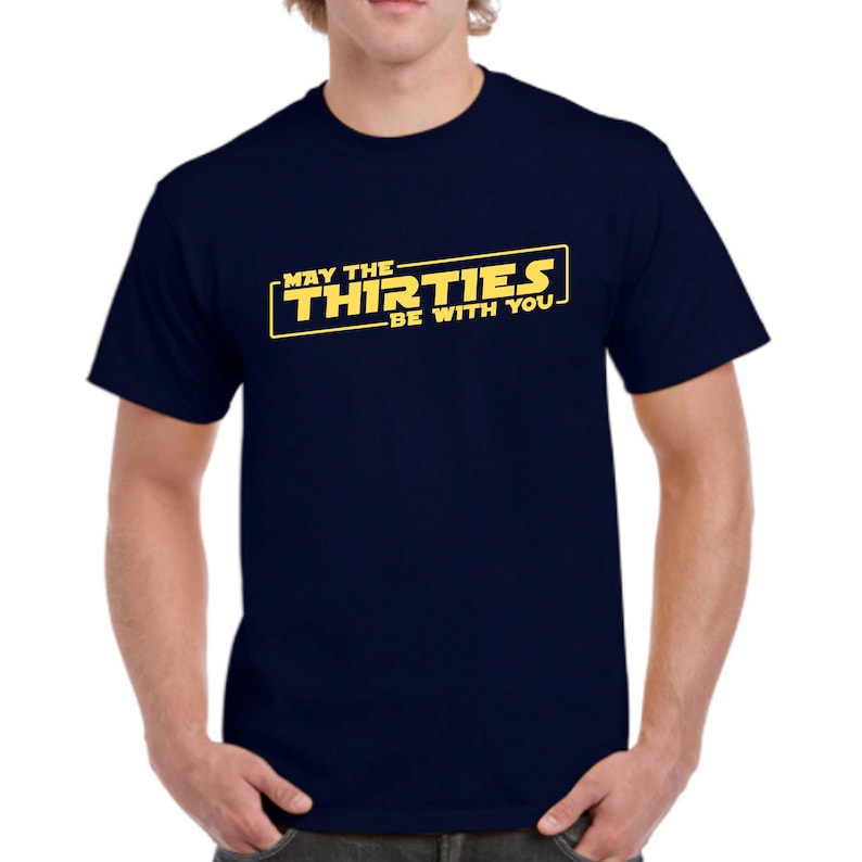 May include: A navy blue t-shirt with a yellow graphic that says "May the Thirties Be With You".