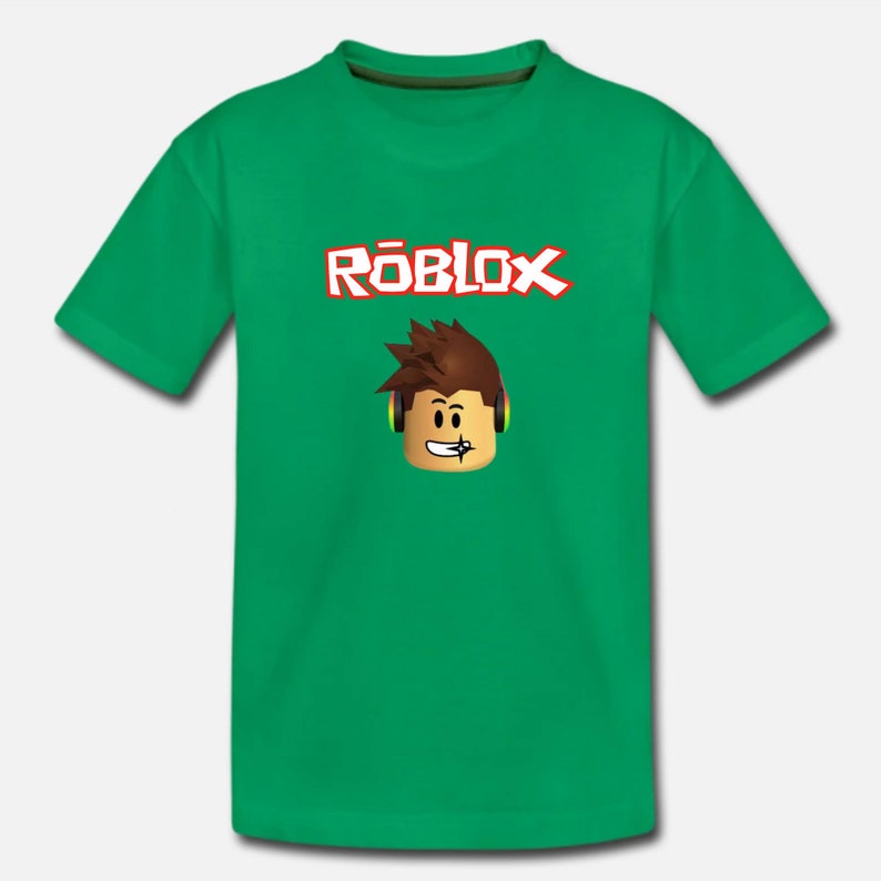 Puede incluir: Camiseta verde con un logotipo de Roblox y un personaje de dibujos animados con auriculares. El logotipo es en rojo y blanco con la palabra "Roblox" en una fuente estilizada.