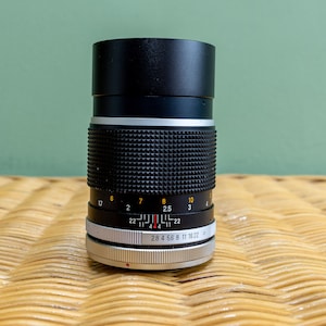 Puede incluir: Un objetivo Canon FD 50 mm f/1.4 negro con un anillo plateado y una tapa de objetivo negra. El objetivo tiene una escala de profundidad de campo y un anillo de apertura con marcas para f/1.4, f/2, f/2.8, f/4, f/5.6, f/8, f/11, f/16 y f/22.