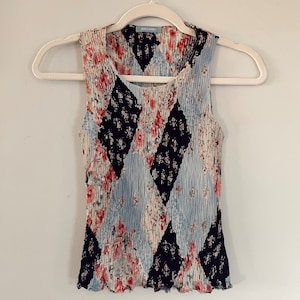May include: A sleeveless, black, blue and pink floral print top with a diamond pattern. The top has a ruffled hem and a small tag that reads "TIKA & MARTA".