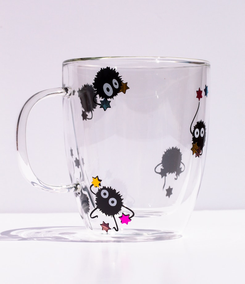 May include: A clear glass mug with a double wall design features black and white illustrations of a cartoon character with stars. The character is surrounded by colorful stars.