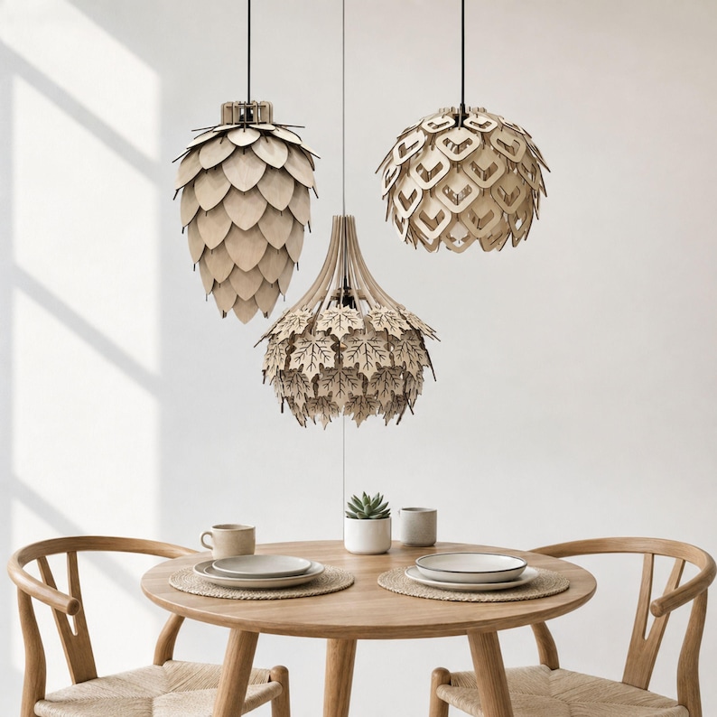 Set of three handcrafted wooden pendant lights featuring layered pinecone, geometric petal, and maple leaf designs, hanging above a Scandinavian Japandi dining table in a minimalist modern dining room with natural oak furniture.