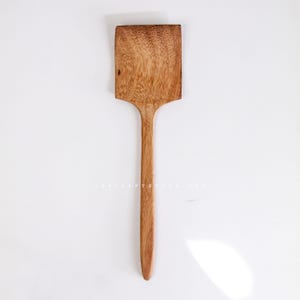 May include: A wooden spatula with a square head and a long, thin handle. The spatula is made of light brown wood and has a natural finish.
