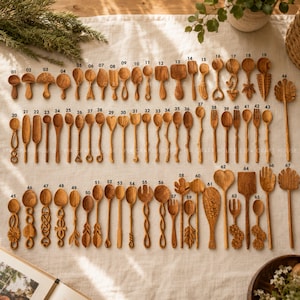 Handcrafted teak wooden spoons and salad utensils in unique carved shapes including hearts, leaves, and fish, laid out and numbered for custom kitchenware selection.