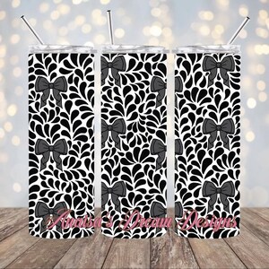 May include: Three stainless steel tumblers with a black and white pattern of stylized bows and droplets. The tumblers are all the same size and have a straw in each.