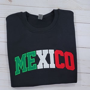 May include: Black sweatshirt with the word "MEXICO" in green, white, and red letters, resembling the colors of the Mexican flag.