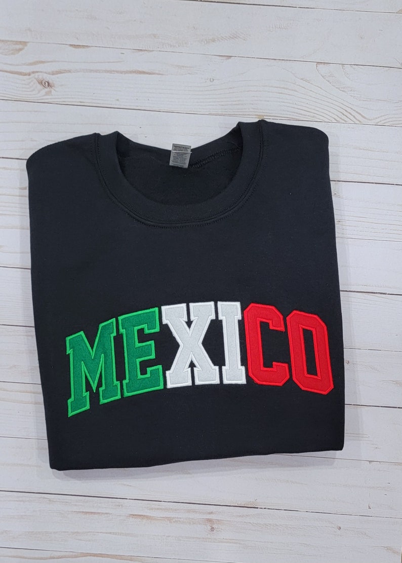 May include: Black sweatshirt with the word "MEXICO" in green, white, and red letters, resembling the colors of the Mexican flag.