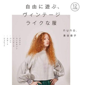 May include: A woman with long curly red hair wears a light gray vintage-style blouse with puffed sleeves and a green skirt. The text "自由に遊ぶ、ヴィンテージライクな服" is written in Japanese above her head. The text "nuno." and "泉谷恭子" is written in Japanese below her.