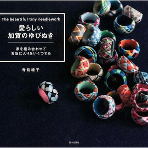 May include: A collection of colourful, handmade finger thimbles, known as "yubi-nuki" in Japanese, with intricate patterns and designs. The thimbles are made of fabric and are used for needlework. The text on the cover reads "The beautiful tiny needlework, 愛らしい 加賀のゆびぬき, 糸を組み合わせて お気に入りをいくつでも, 寺島綾子, 日本文芸社".