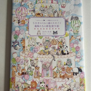 May include: A colorful children's coloring book featuring numerous cartoon animals, including cats, pandas, and elephants, arranged on a multi-tiered cake design. The book cover has Japanese text and is decorated with balloons and hot air balloons.