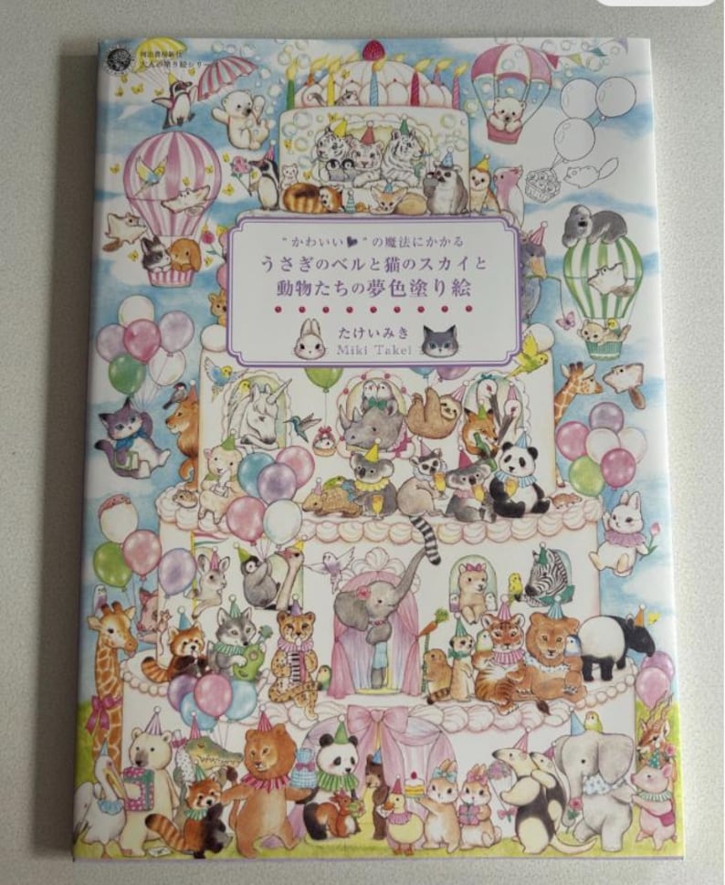 May include: A colorful children's coloring book featuring numerous cartoon animals, including cats, pandas, and elephants, arranged on a multi-tiered cake design. The book cover has Japanese text and is decorated with balloons and hot air balloons.
