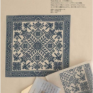 May include: A page from a cross-stitch pattern book featuring a detailed blue and white floral design. The design includes birds and geometric shapes. The text "Thistle Birds" is visible, along with Japanese text and a small envelope with a handwritten note.