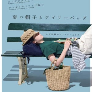 May include: A craft book cover featuring a light blue background with Japanese text, a person wearing a tan straw hat, a green t-shirt, and striped pants, lying on a dark green bench with a tan woven straw tote bag hanging from their arm.