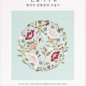 May include: A book cover with a light mint green square containing a circular embroidery design of pink, red, and yellow flowers and birds. The text reads "전통자수 2", "한국의 전통문양 수놓기", and other Korean characters in black.