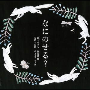 May include: A black and white illustration of a fox and a rabbit jumping over a circle of green branches with blue berries. The text "なにのせる?" is written in Japanese characters in the centre of the image. The text "絵とおさら 鹿児島睦" is written in Japanese characters below the image. The text "お話と企画 ギャラリーフェプ" is written in Japanese characters below the image. The text "文化出版局" is written in Japanese characters at the bottom of the image.