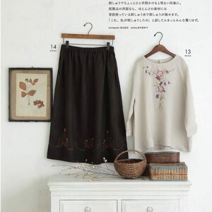 May include: A black skirt and a light-colored long-sleeve shirt with floral embroidery hang on a wooden rack. A framed botanical print and a woven basket sit on a white dresser. The image features Japanese text.