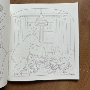 Op de afbeelding: Een zwart-wit kleurboekpagina met een illustratie van een ezel, een hond, een kat en een kip die rond een tafel zitten. Op de tafel staan een grote taart, wijnglazen en eten. De sc&egrave;ne speelt zich af voor een raam met gordijnen en sterren.