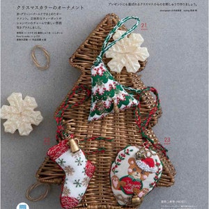 May include: A woven Christmas tree-shaped basket holds several embroidered ornaments. The ornaments include a snowflake, a Christmas tree, a stocking, and a heart-shaped design with a teddy bear. The text in the image says "Christmas" and "Christmas color ornaments".