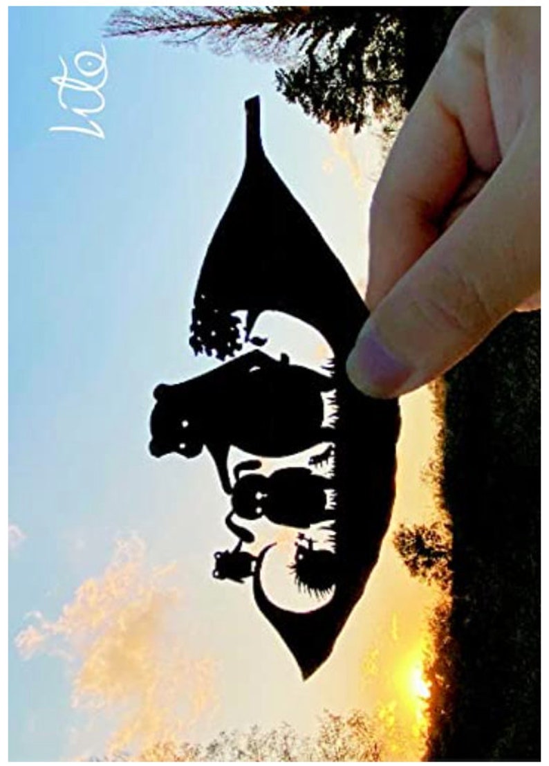May include: A black paper silhouette of a leaf with a family of bears inside. The silhouette is held up against a sunset sky.