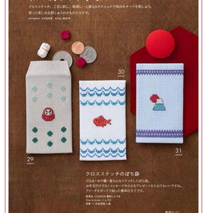 May include: A page from a Japanese craft book featuring cross-stitch designs. The image showcases three small, embroidered pouches with different motifs: a Daruma doll, a red fish, and Mount Fuji. The text includes Japanese characters and instructions.