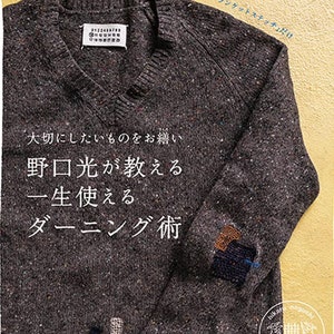 Puede incluir: Primer plano de un suéter gris oscuro con cuello en V y un parche en el codo. El suéter tiene una textura moteada y el texto "大切にしたいものをお繕い 野口光が教える 一生使える ダーニング術" está impreso en la parte delantera.