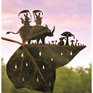 May include: A leaf with a rhino, two rabbits, and mushrooms cut out of it. The leaf is green and has raindrops cut out of it. The background is a pink and purple sky.
