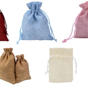 Puede incluir: Cinco bolsas de cordón de arpillera en varios colores. Las bolsas son roja, azul, rosa, marrón y beige.