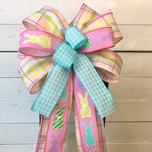May include: A pink and green plaid ribbon bow with a turquoise ribbon in the center. The ribbon has a pattern of colorful Easter bunnies. The bow is tied around a black lantern.