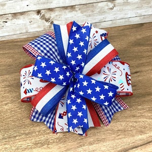 May include: A red, white and blue bow with a gingham pattern, stars and fireworks. The bow is made of ribbon and is perfect for a patriotic celebration.