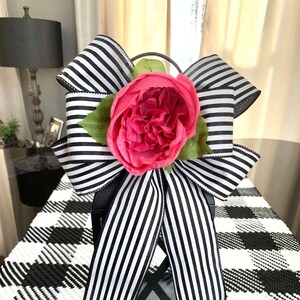 May include: Black and white striped ribbon bow with a pink flower on top of a black lantern. The lantern is sitting on a black and white checkered surface.