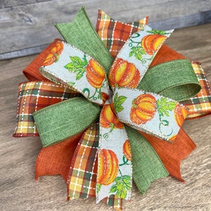 K&ouml;nnte beinhalten: Eine herbstliche Schleife mit gr&uuml;nem, orangefarbenem und braunem kariertem Band, einem gr&uuml;nen Sackleinenband und einem wei&szlig;en Band mit K&uuml;rbisdruck.