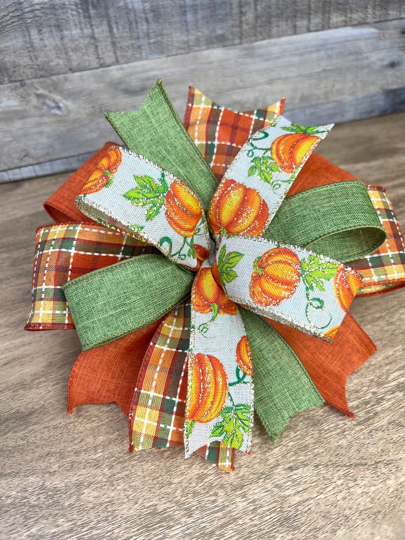 K&ouml;nnte beinhalten: Eine herbstliche Schleife mit gr&uuml;nem, orangefarbenem und braunem kariertem Band, einem gr&uuml;nen Sackleinenband und einem wei&szlig;en Band mit K&uuml;rbisdruck.