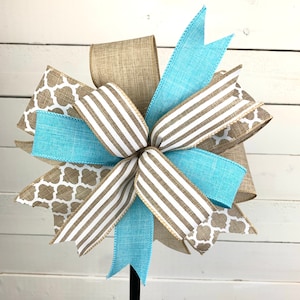 May include: A decorative bow made with brown and blue ribbon. The bow is made with a variety of patterns, including stripes, geometric designs, and burlap. The bow is tied to a black stick.