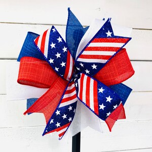 May include: A red, white, and blue patriotic bow with a star-spangled design. The bow is made of fabric and is tied with a ribbon. It is perfect for decorating for the Fourth of July or other patriotic holidays.