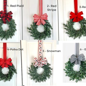 May include: Six decorative wreaths with green foliage and various red ribbon designs. The ribbons include red plaid, red stripe, red velvet, polka dot, snowman, and gingham patterns. Each wreath is hung on a white door.