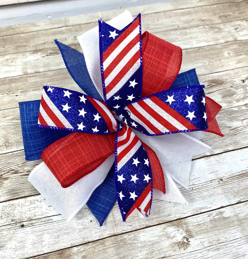 May include: A red, white, and blue bow with glitter stars and stripes. The bow is made of burlap and ribbon.