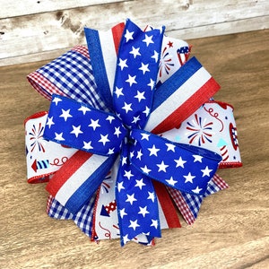 May include: A red, white and blue bow made with various patterned ribbons, including gingham, stars and fireworks. The bow is perfect for a patriotic celebration.